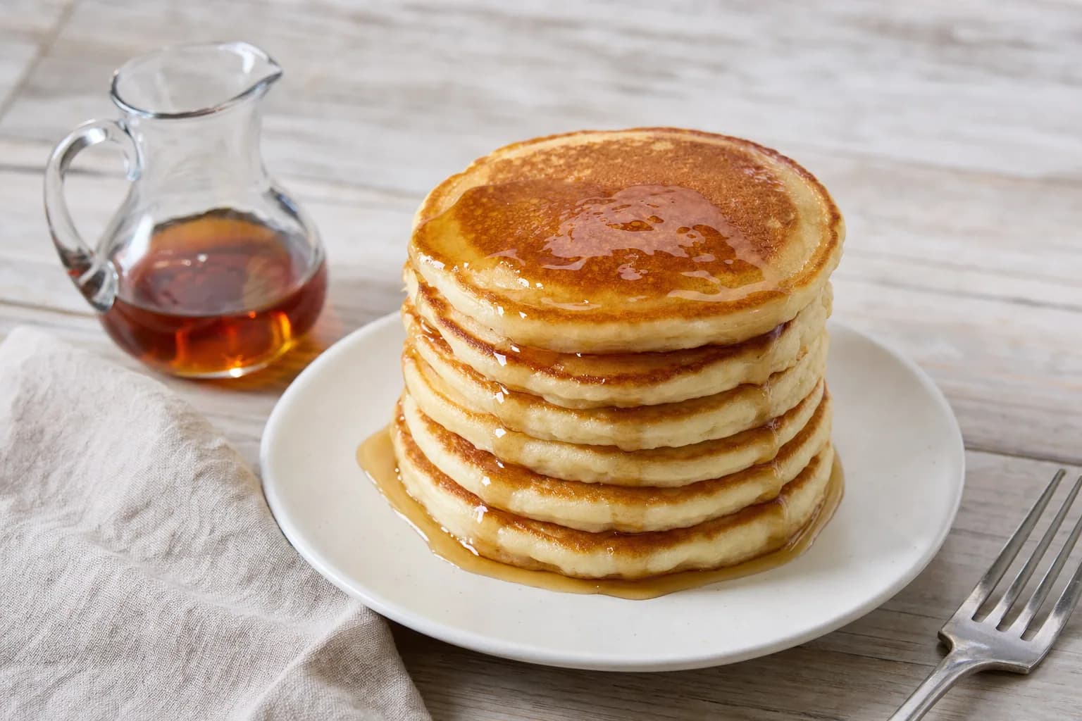A tall stack of golden gluten-free buttermilk pancakes with maple syrup dripping down the sides.